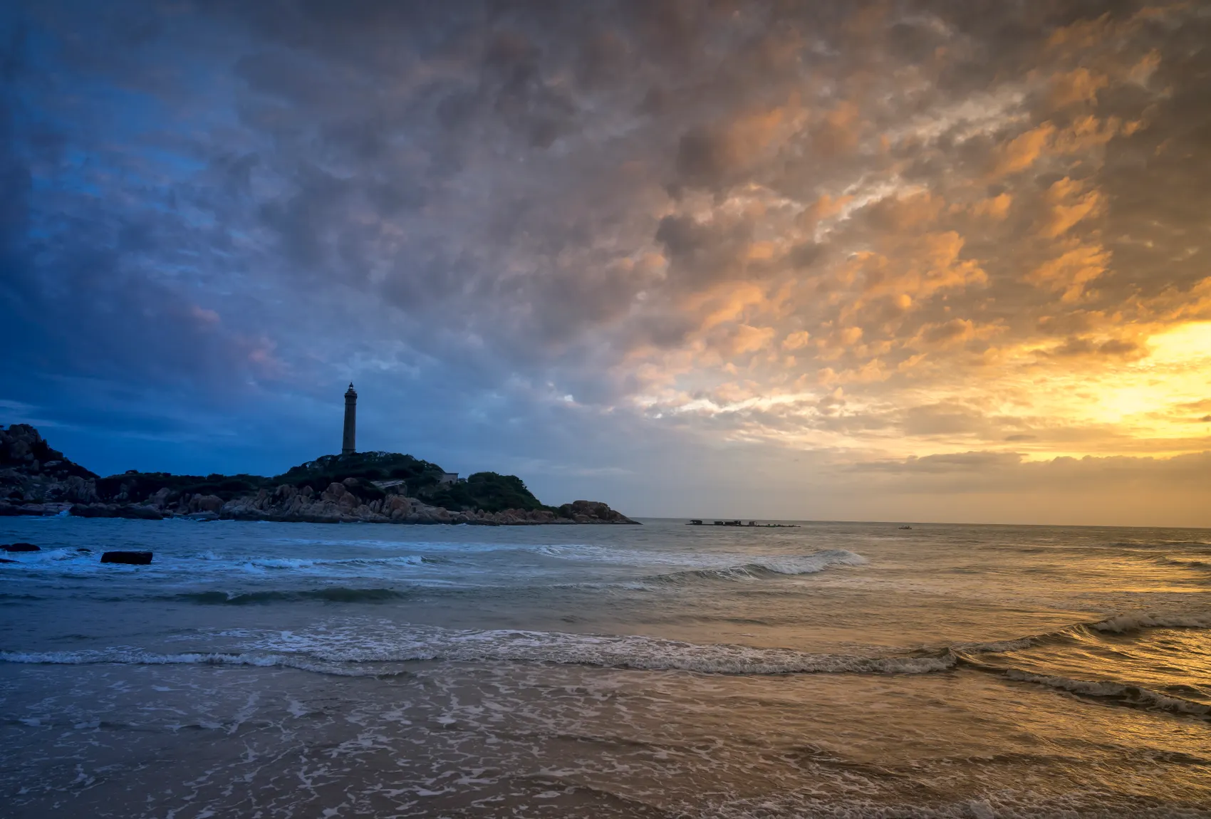 Faro recortado sobre el cielo del atardecer en una playa de mar abierto
